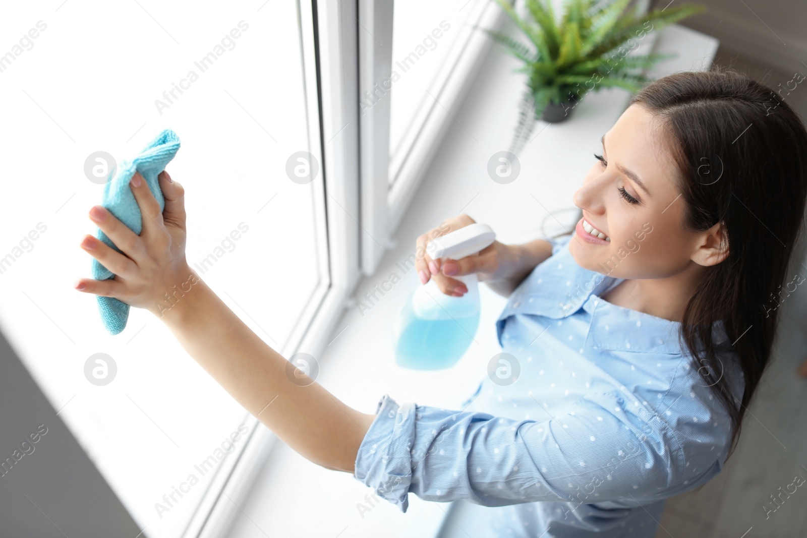 Photo of Young woman cleaning window glass at home