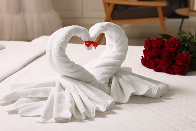 Photo of Honeymoon. Swans made of towels and beautiful red roses on bed in room