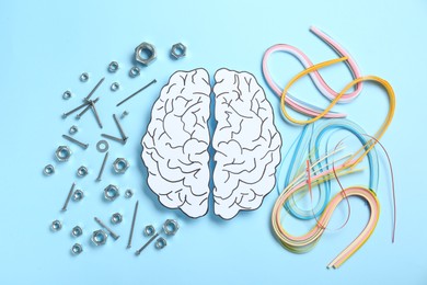 Photo of Creativity and logic. Paper brain on light blue background, flat lay. Screws with nuts near left hemisphere and quilling strips near right one