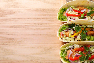 Photo of Delicious fish tacos served on wooden table, top view with space for text