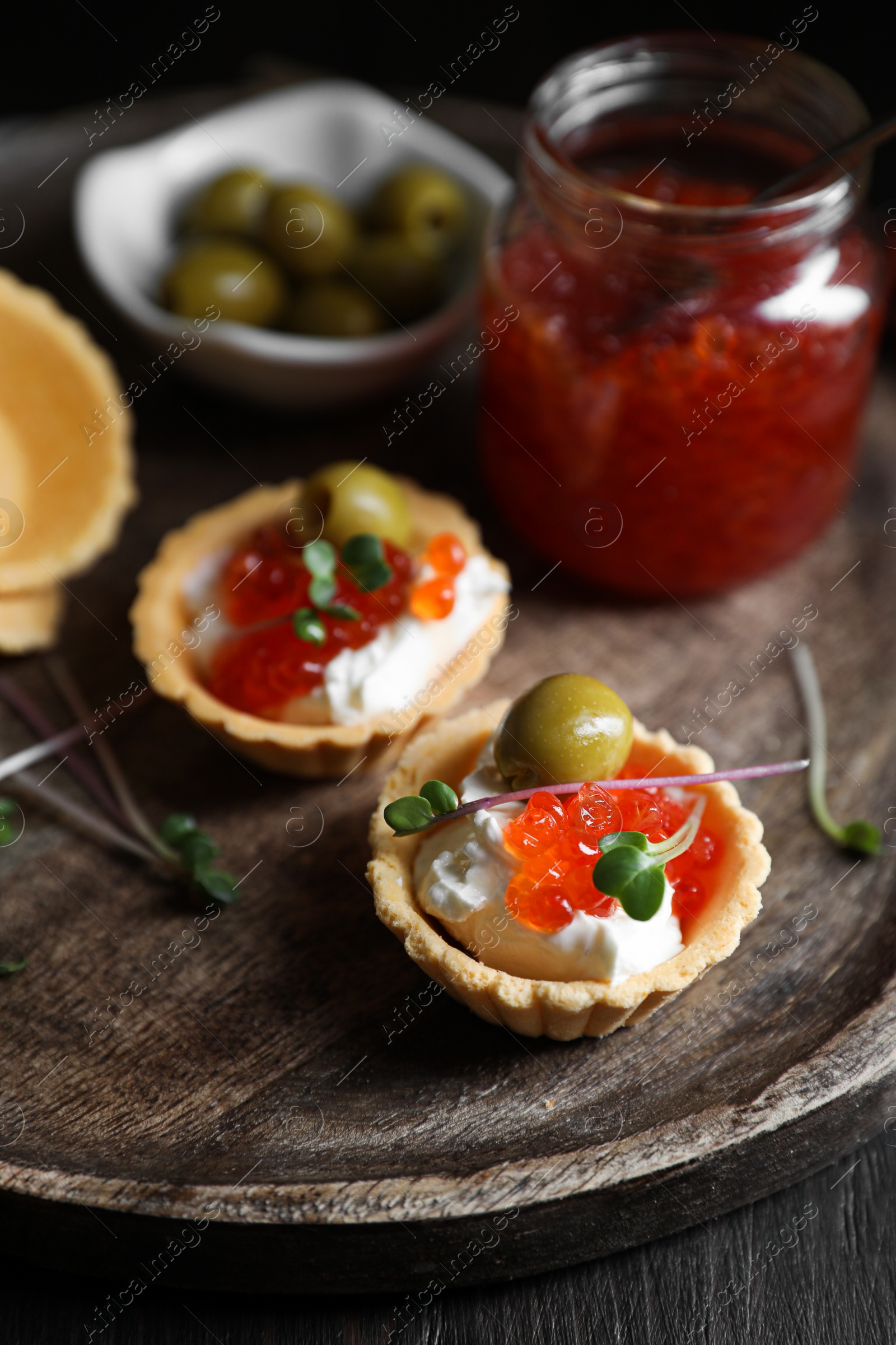 Photo of Delicious tartlets with red caviar and cream cheese served on wooden table, closeup