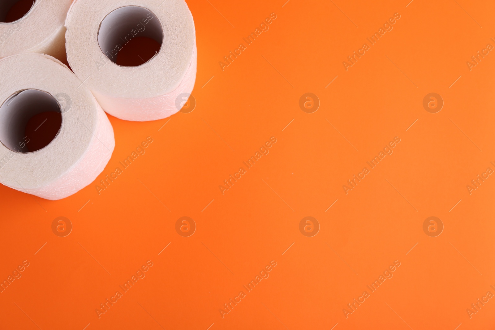 Photo of Soft toilet paper rolls on orange background, above view. Space for text