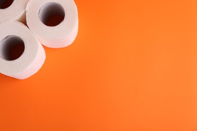 Soft toilet paper rolls on orange background, above view. Space for text