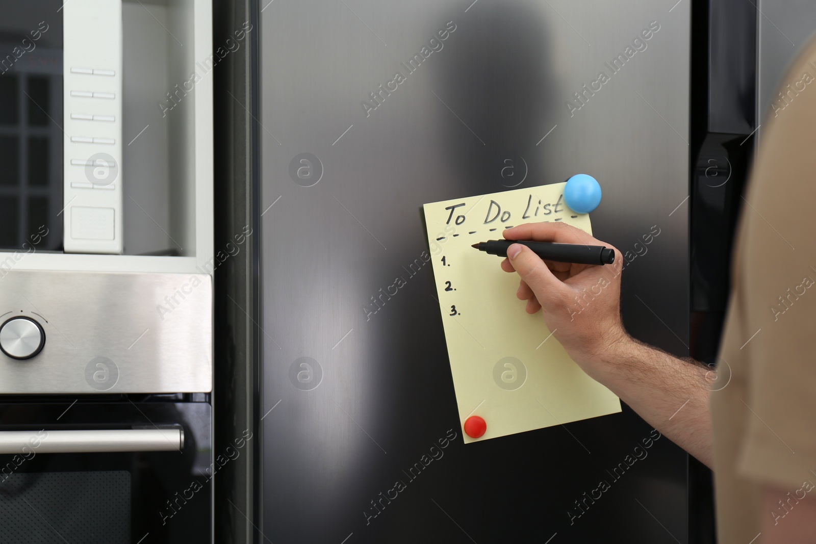 Photo of Man writing to do list on refrigerator door in kitchen, closeup. Space for text