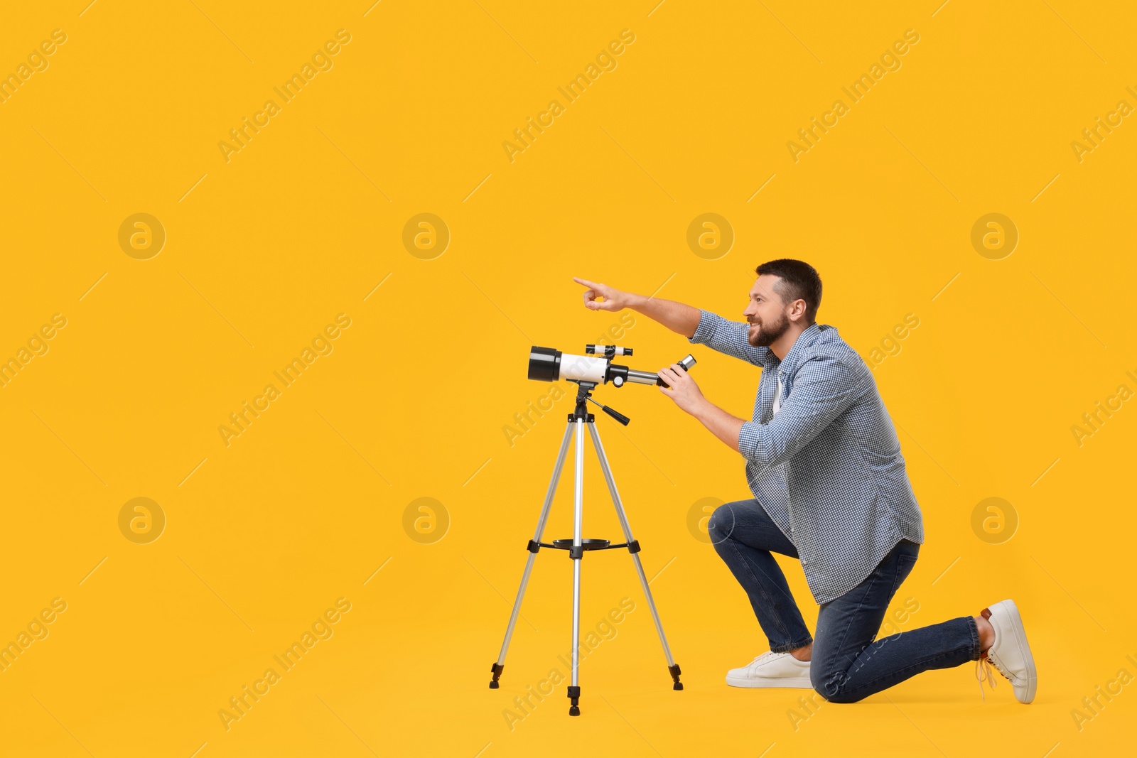 Photo of Happy astronomer with telescope pointing at something on orange background. Space for text