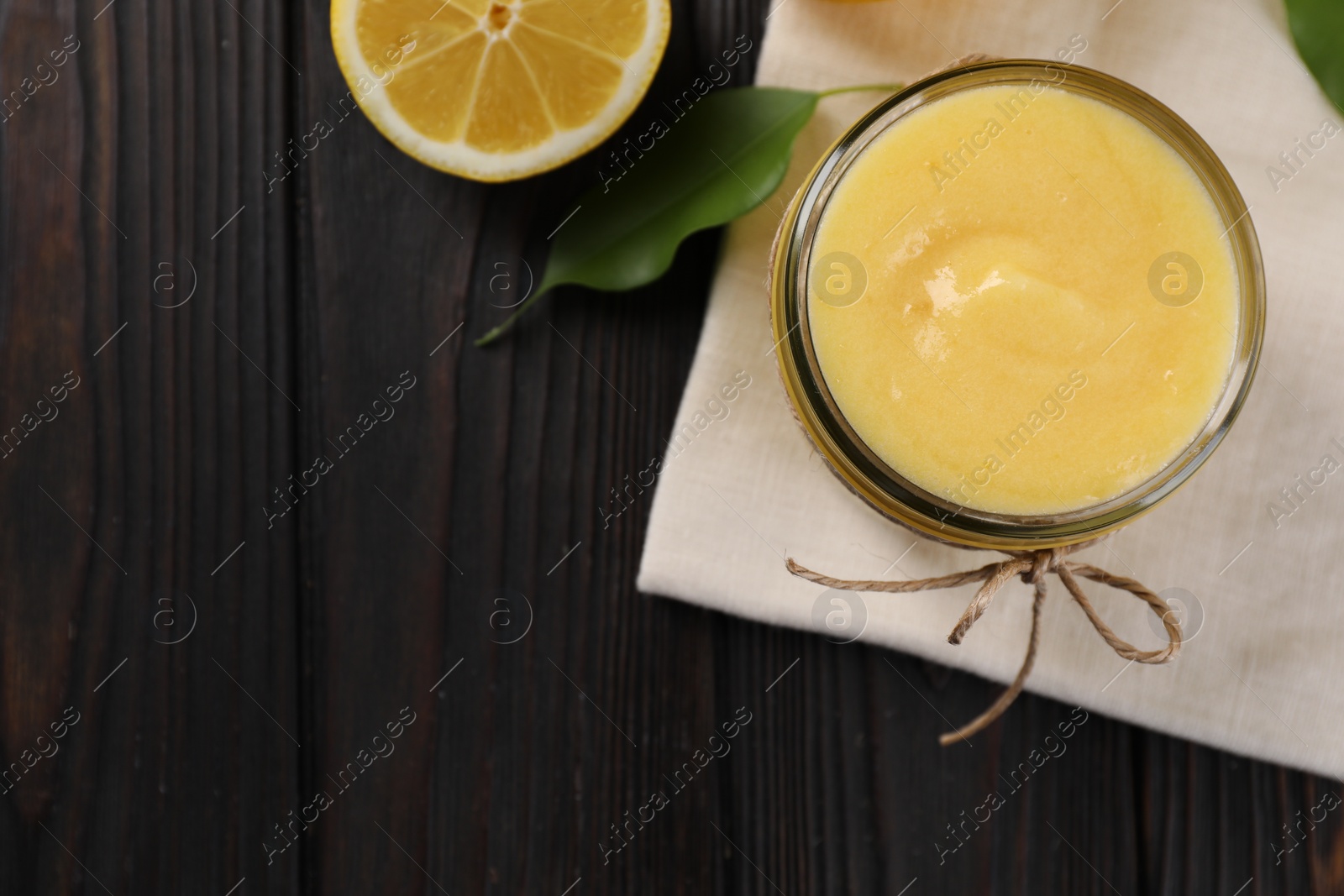 Photo of Delicious lemon curd in bowl, fresh citrus fruit and green leaf on wooden table, top view. Space for text