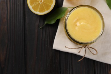 Delicious lemon curd in bowl, fresh citrus fruit and green leaf on wooden table, top view. Space for text