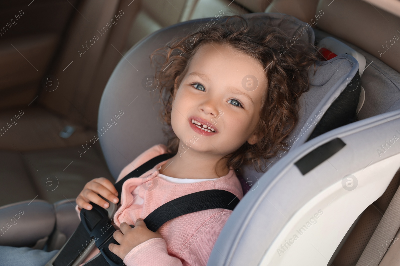 Photo of Cute little girl sitting in child safety seat inside car