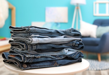 Photo of Stack of stylish jeans on table against blurred background