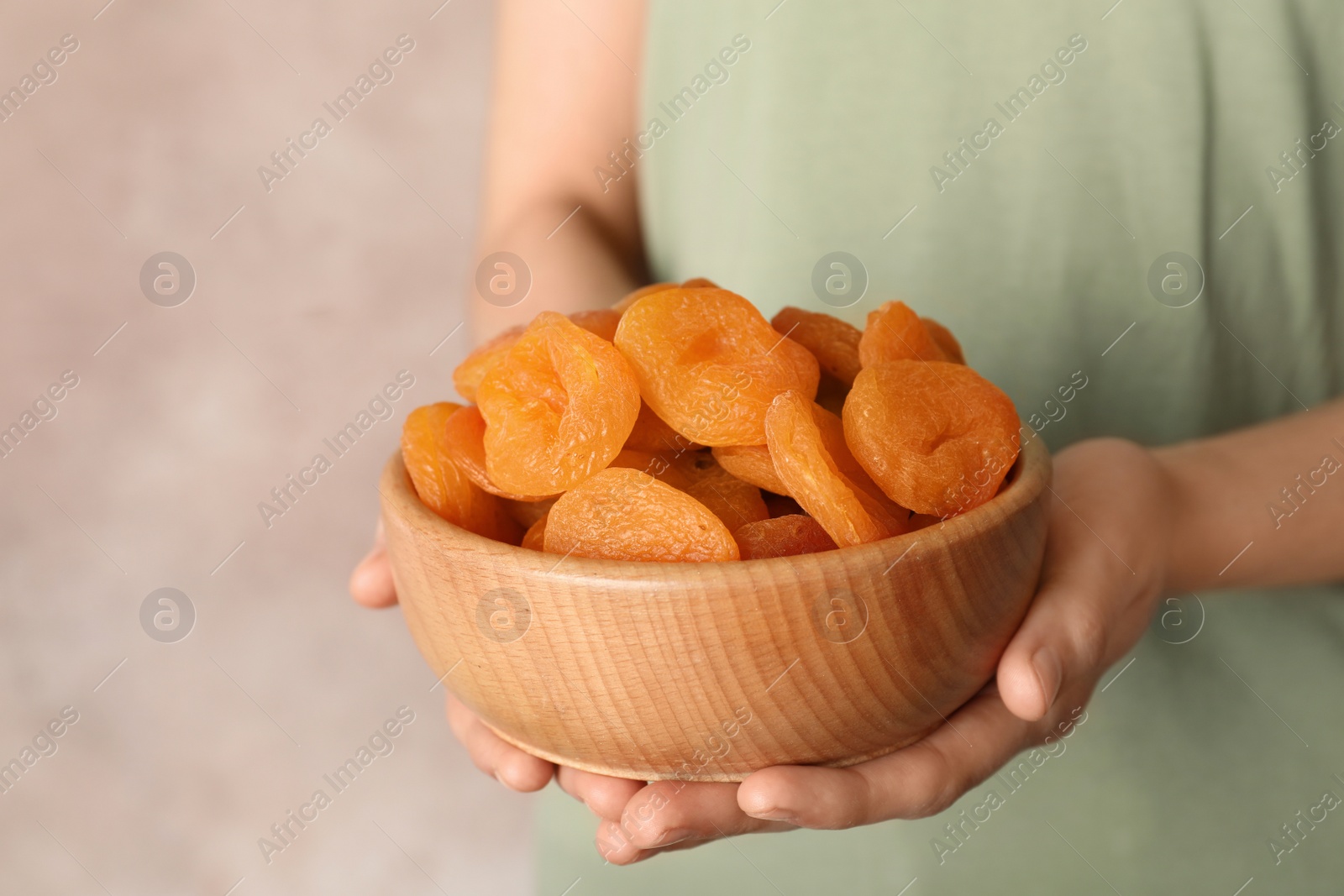 Photo of Woman holding bowl with dried apricots on color background, space for text. Healthy fruit