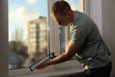 Construction worker sealing window with caulk indoors