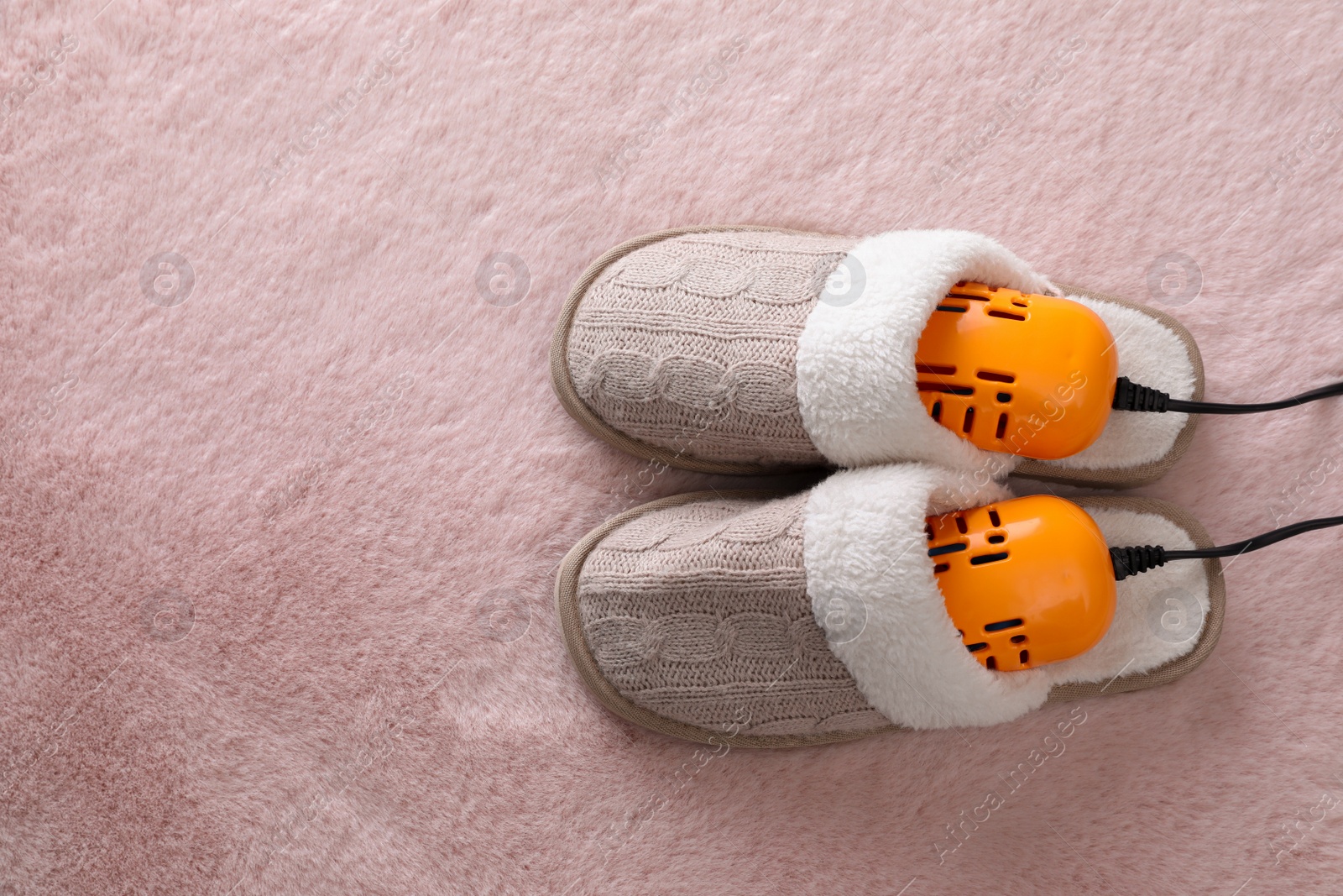 Photo of Pair of soft slippers with modern electric footwear dryer on pink carpet, top view. Space for text