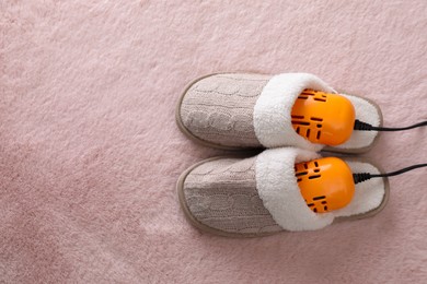 Photo of Pair of soft slippers with modern electric footwear dryer on pink carpet, top view. Space for text