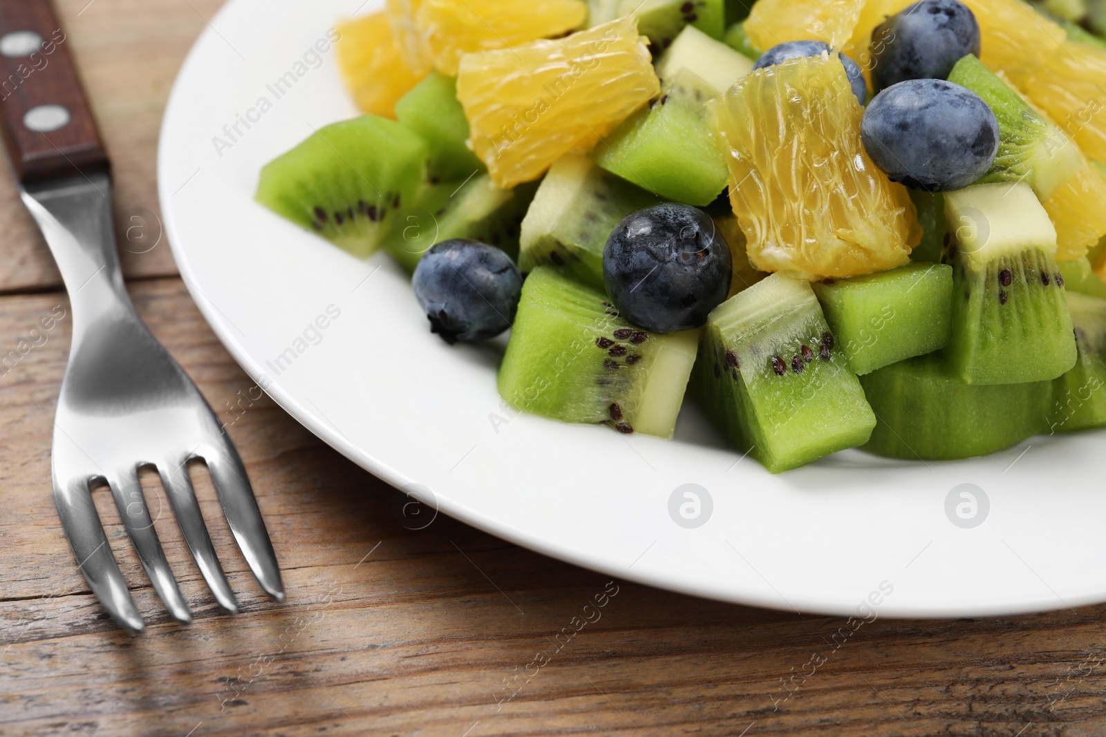 Photo of Plate of tasty fruit salad and fork on wooden table, closeup