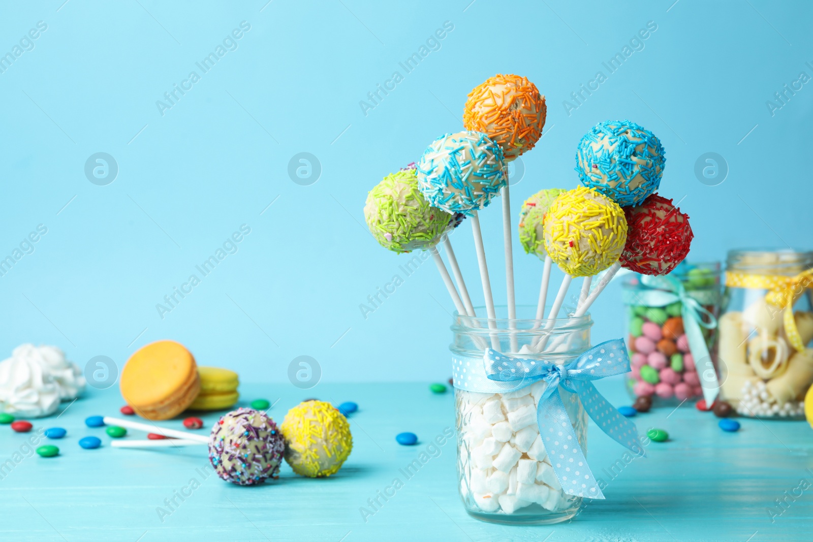 Photo of Yummy bright cake pops in glass jar full of marshmallows on table. Space for text