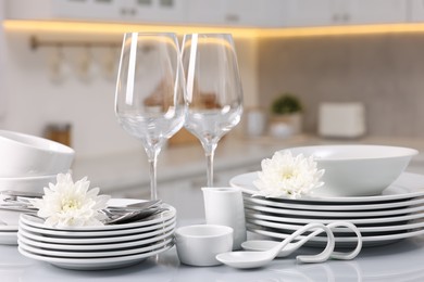 Photo of Set of clean dishware, glasses, cutlery and flowers on table in kitchen