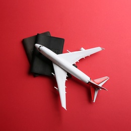 Toy airplane and passports on red background, flat lay