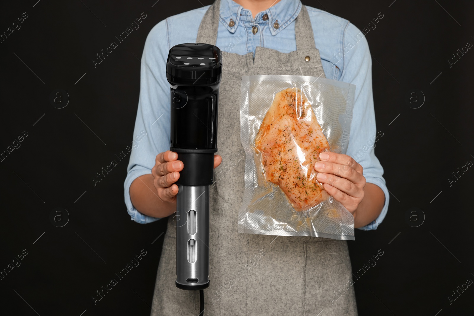 Photo of Woman holding sous vide cooker and meat in vacuum pack on black background, closeup