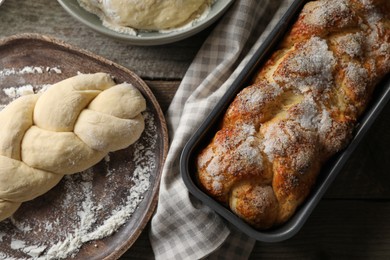 Photo of Fresh dough with flour and tasty braided bread on wooden table, flat lay. Traditional Shabbat challah
