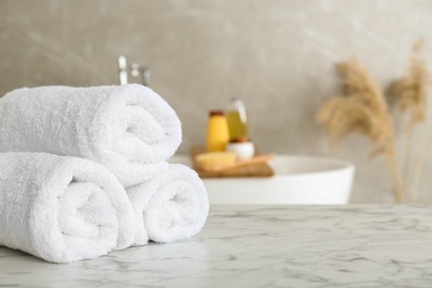 Photo of Rolled bath towels on white marble table in bathroom, space for text