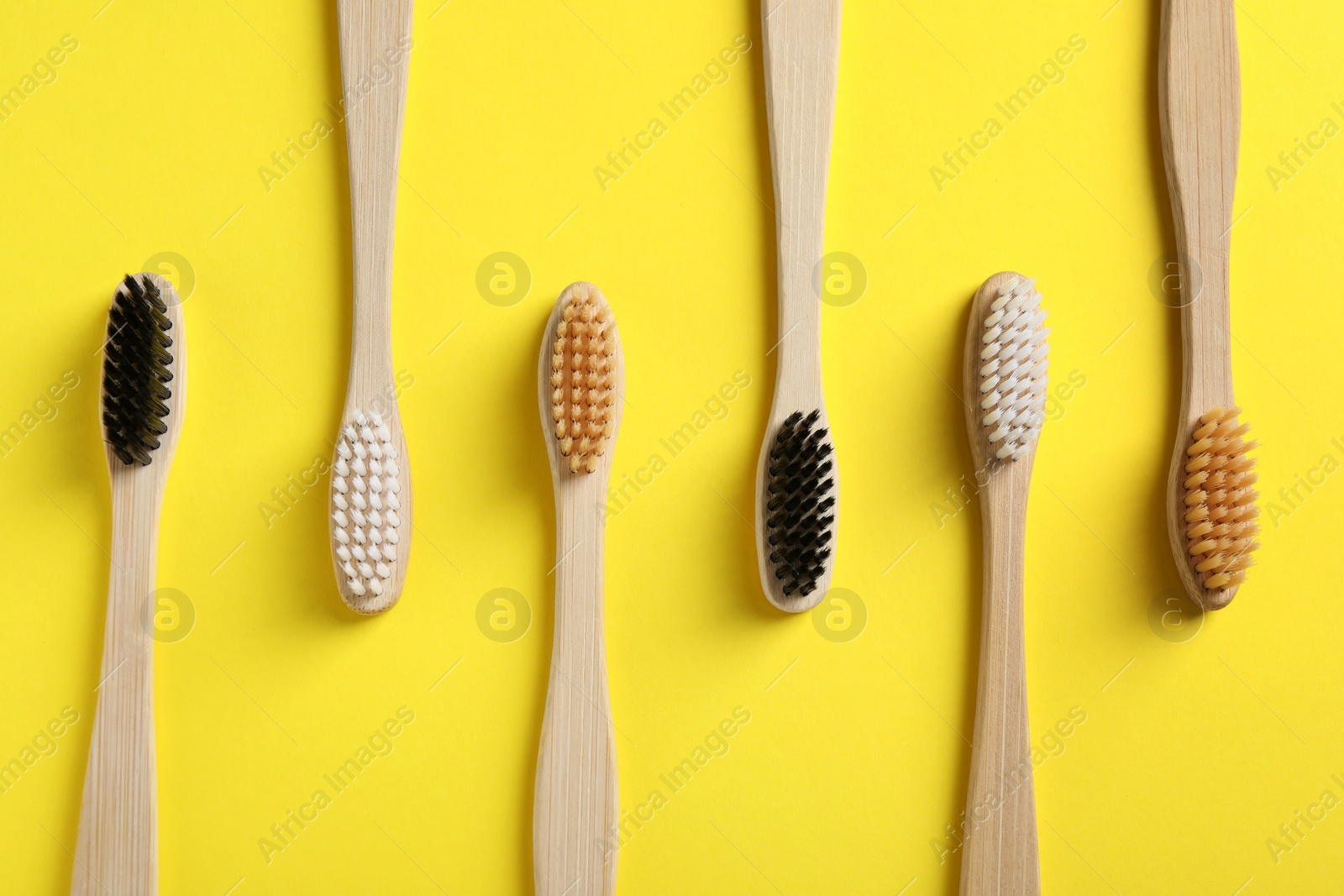 Photo of Bamboo toothbrushes on yellow background, flat lay
