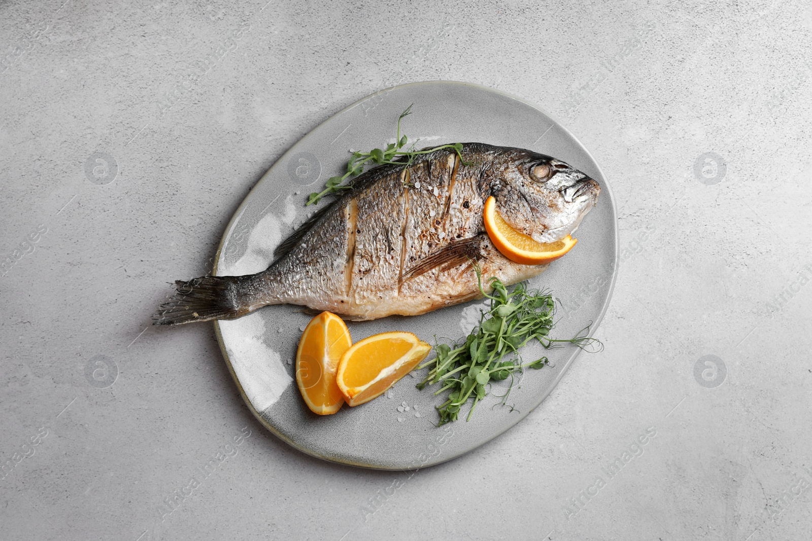 Photo of Seafood. Delicious baked fish served with orange and microgreens on light textured table, top view