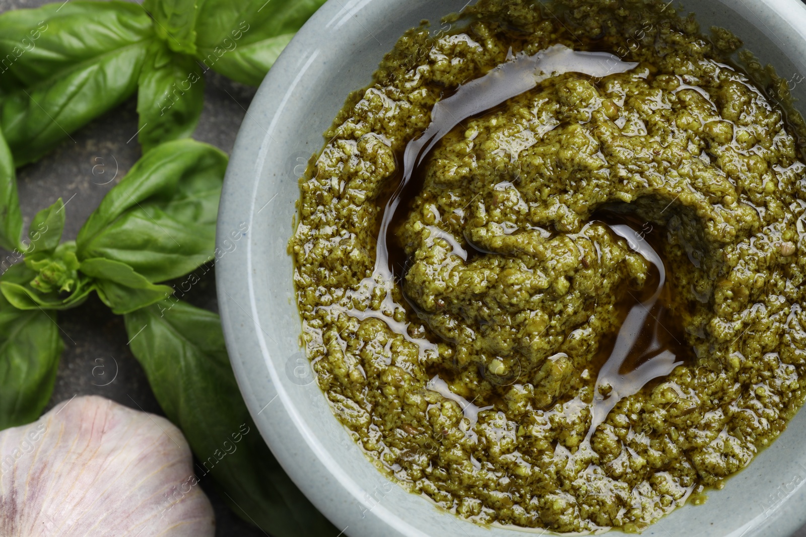 Photo of Tasty pesto sauce in bowl, basil and garlic on table, top view