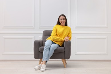 Photo of Beautiful woman sitting in armchair near white wall indoors