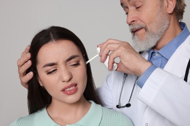 Photo of Doctor spraying medication into woman's ear on light grey background, closeup