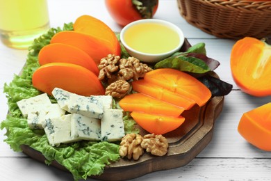 Photo of Delicious persimmon, blue cheese, nuts and honey served on white wooden table