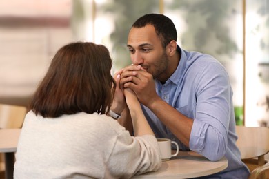 Photo of Romantic date. Guy kissing his girlfriend's hands in cafe