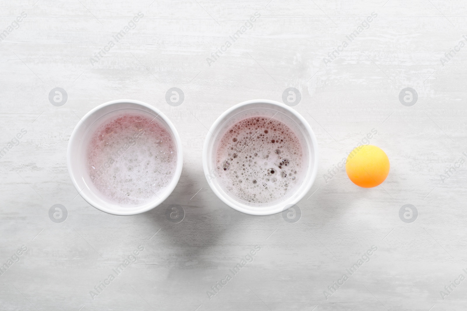 Photo of Plastic cups and ball for beer pong on white table, flat lay
