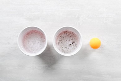 Plastic cups and ball for beer pong on white table, flat lay