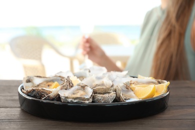 Photo of Fresh oysters with cut juicy lemon and woman at table