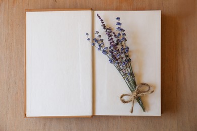 Photo of Open book with bunch of dried flowers on wooden table, top view