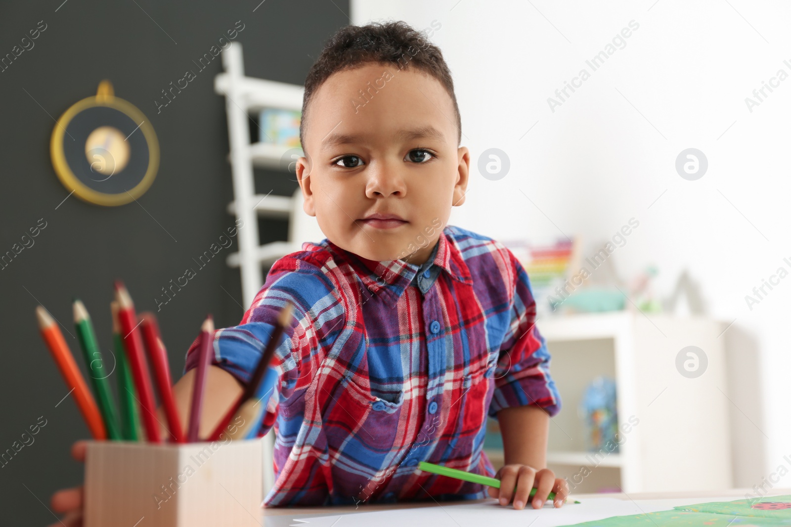 Photo of Cute little African-American child drawing at table in kindergarten. Indoor activity