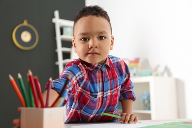 Photo of Cute little African-American child drawing at table in kindergarten. Indoor activity