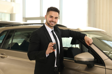 Young salesman with key near car in dealership