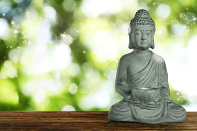 Image of Stone Buddha sculpture on wooden table outdoors. Space for text
