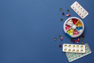 Plastic box with different pills on blue background, flat lay. Space for text