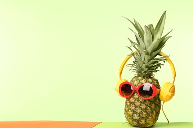 Photo of Funny pineapple with headphones and sunglasses on color background, space for text