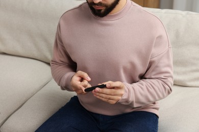 Diabetes test. Man checking blood sugar level with lancet pen on sofa, closeup