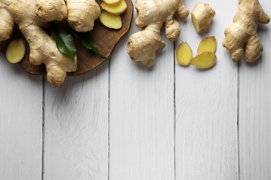 Cut and whole fresh ginger with leaves on white wooden table, flat lay. Space for text