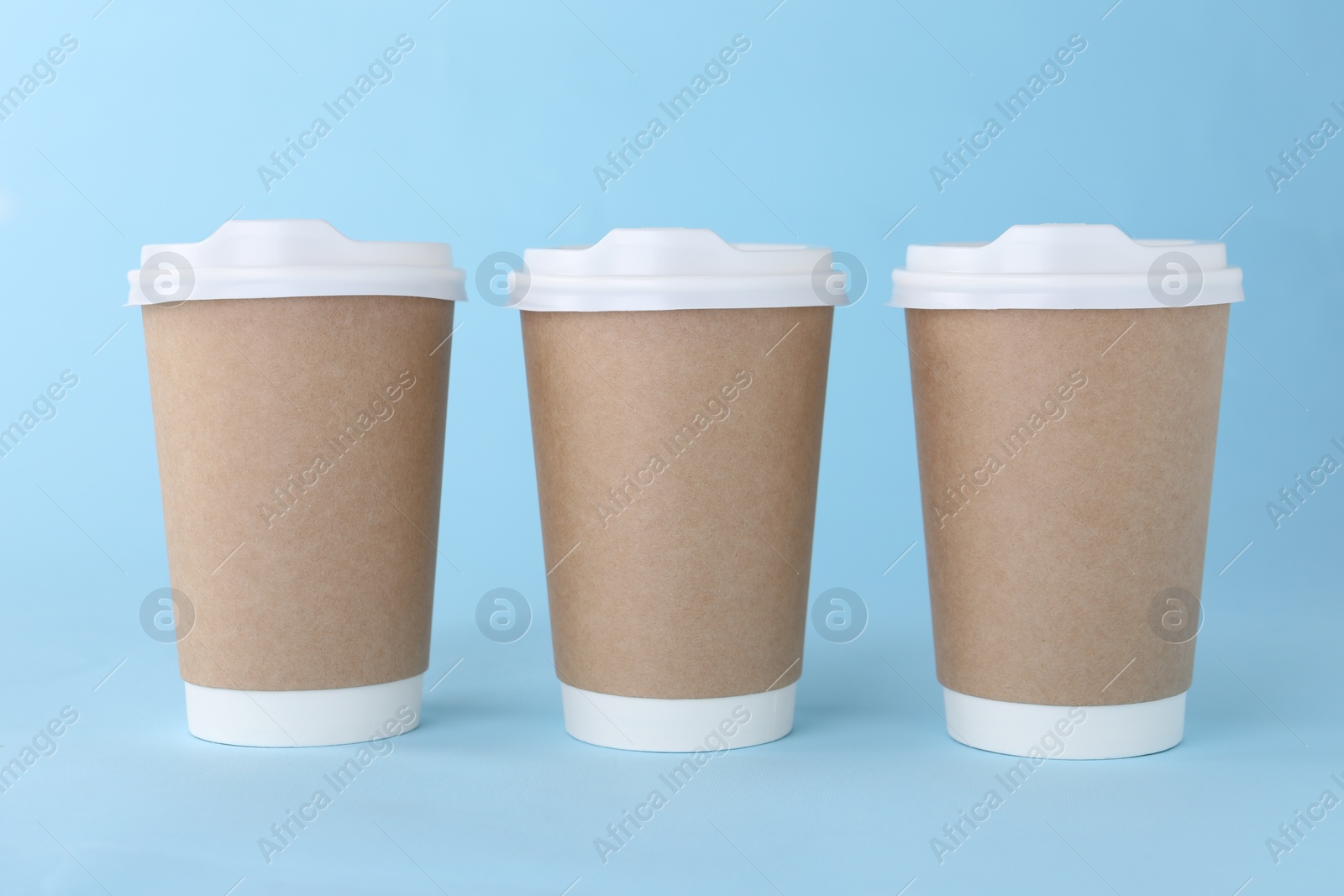 Photo of Paper cups with white lids on light blue background. Coffee to go