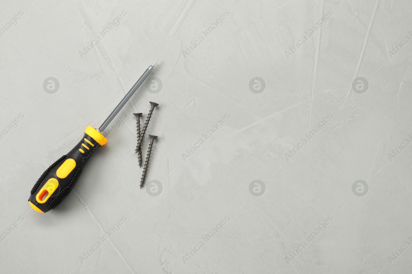 Photo of Screwdriver with black handle and screws on grey table, flat lay. Space for text