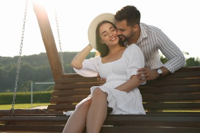 Photo of Romantic date. Beautiful couple spending time together on swing bench outdoors