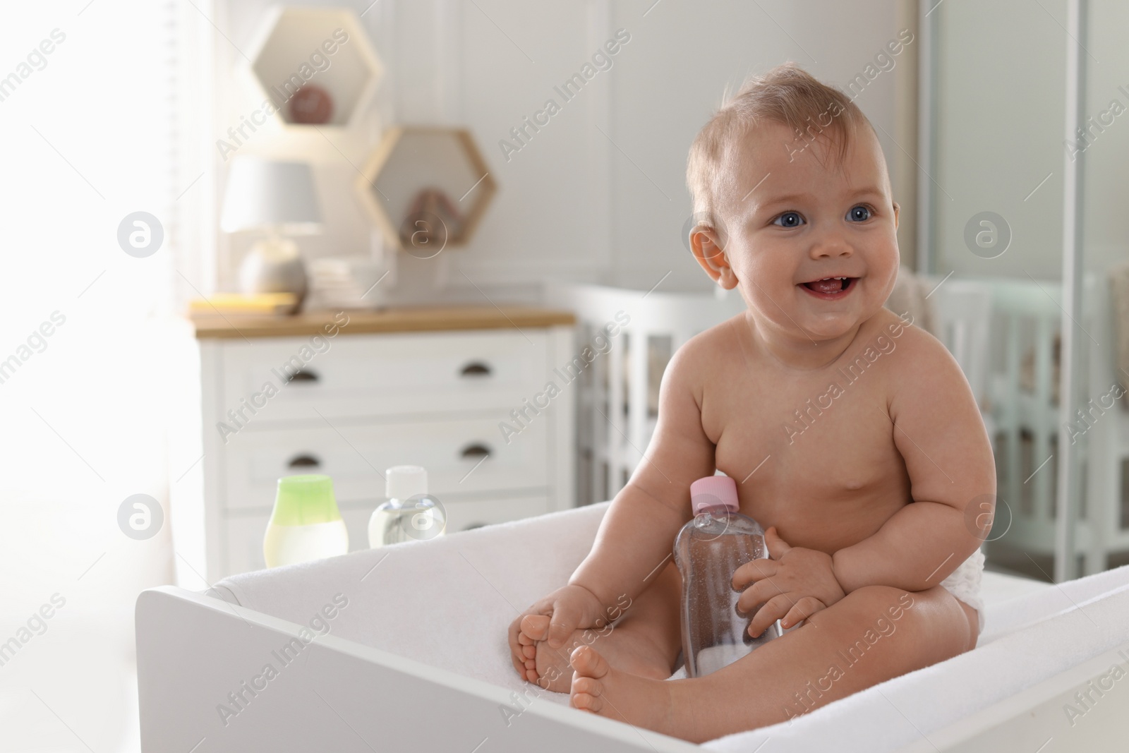 Photo of Cute little baby with bottle of massage oil on changing table at home