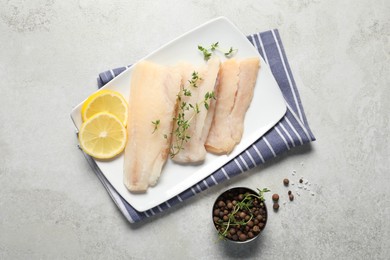 Photo of Pieces of raw cod fish, peppercorns and lemon on light grey table, top view