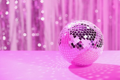 Shiny disco ball on table against blurred background, toned in pink. Space for text