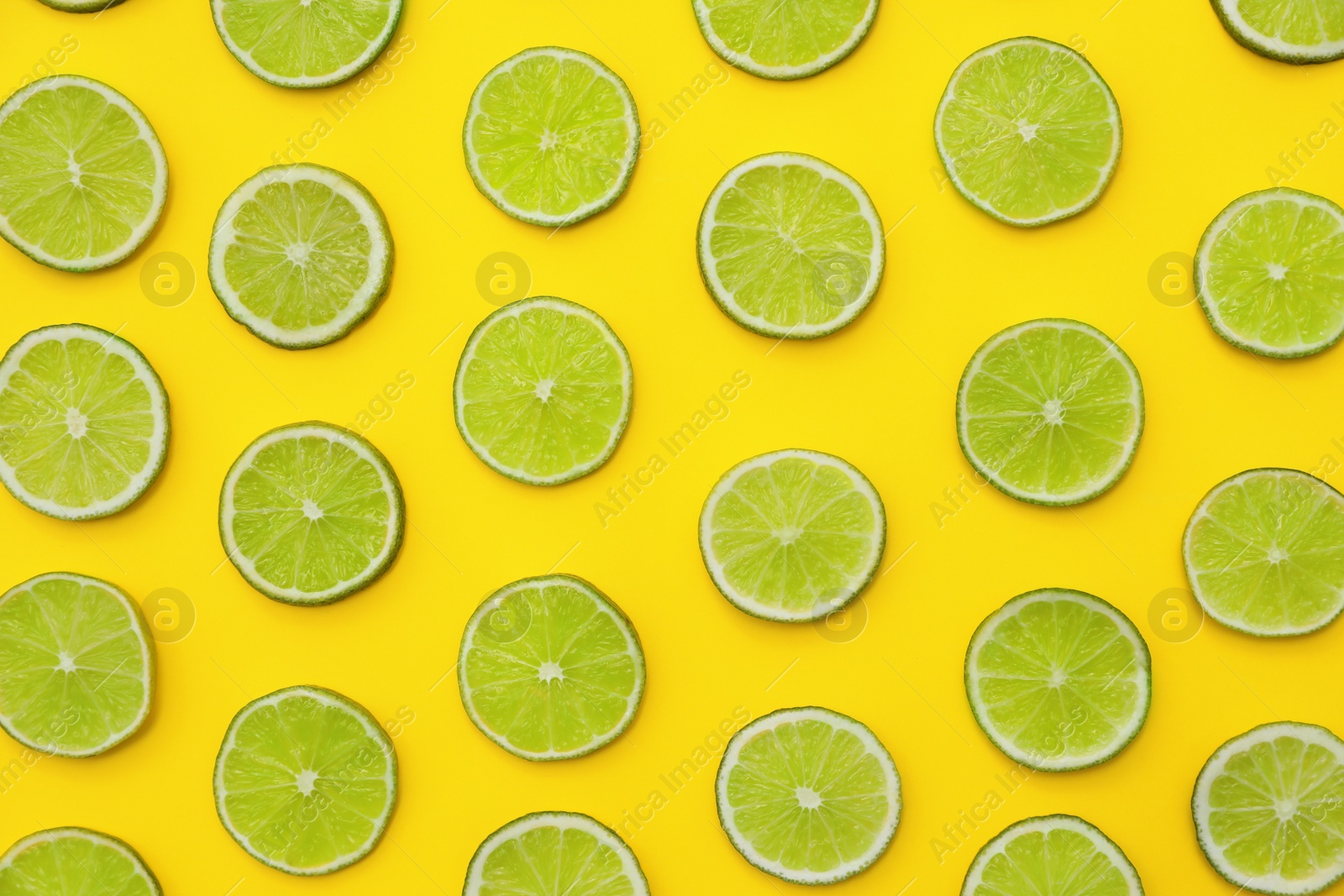 Photo of Slices of fresh juicy limes on yellow background, flat lay